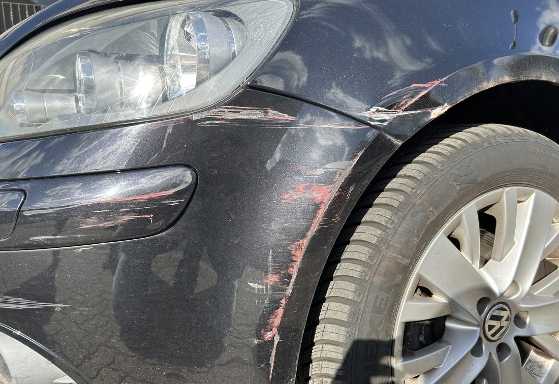 Eingedrückter vorderer Kotflügel eines schwarzen VW Golf Plus mit roten Lackantragungen des Unfallgegners, wirtschaftlicher Totalschaden
