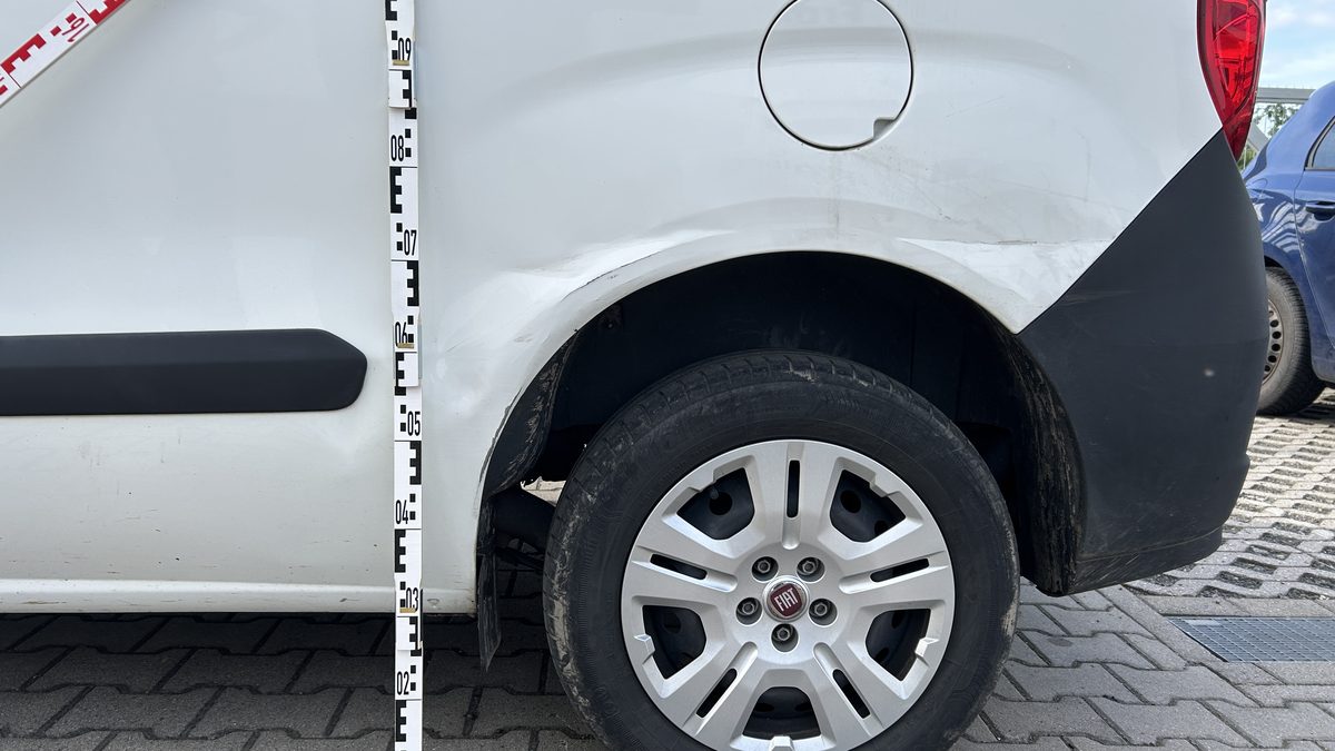 Schadenaufnahme an einem weißen Kastenwagen, Eindrückung an der hinteren Seitenwand mit zwei Messlatten dokumentiert